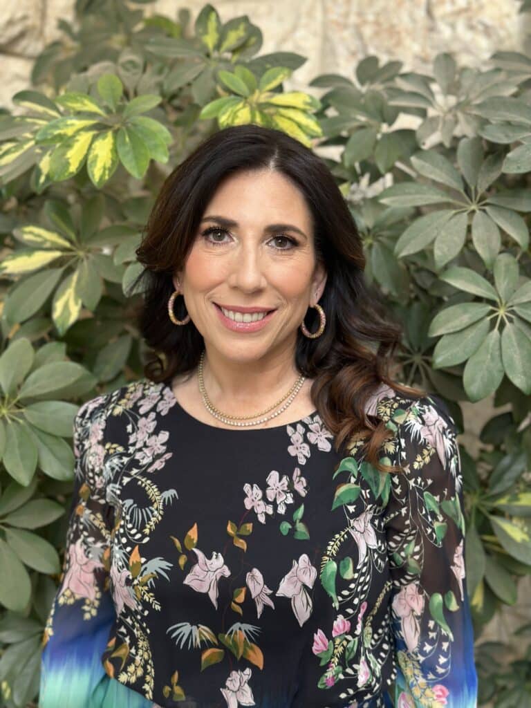 May contain a person wearing a black floral top with earrings and a necklace.