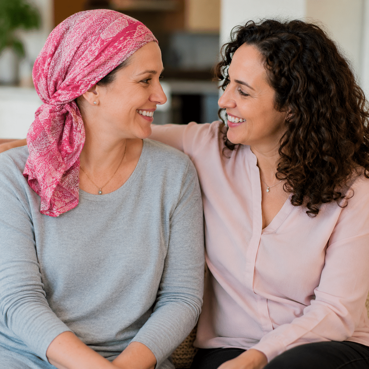 Two women sit at a table having a serious conversation about Jewish breast cancer support. One gestures with her hand while the other listens. Papers, a notebook, and a mug are on the table in front of them.